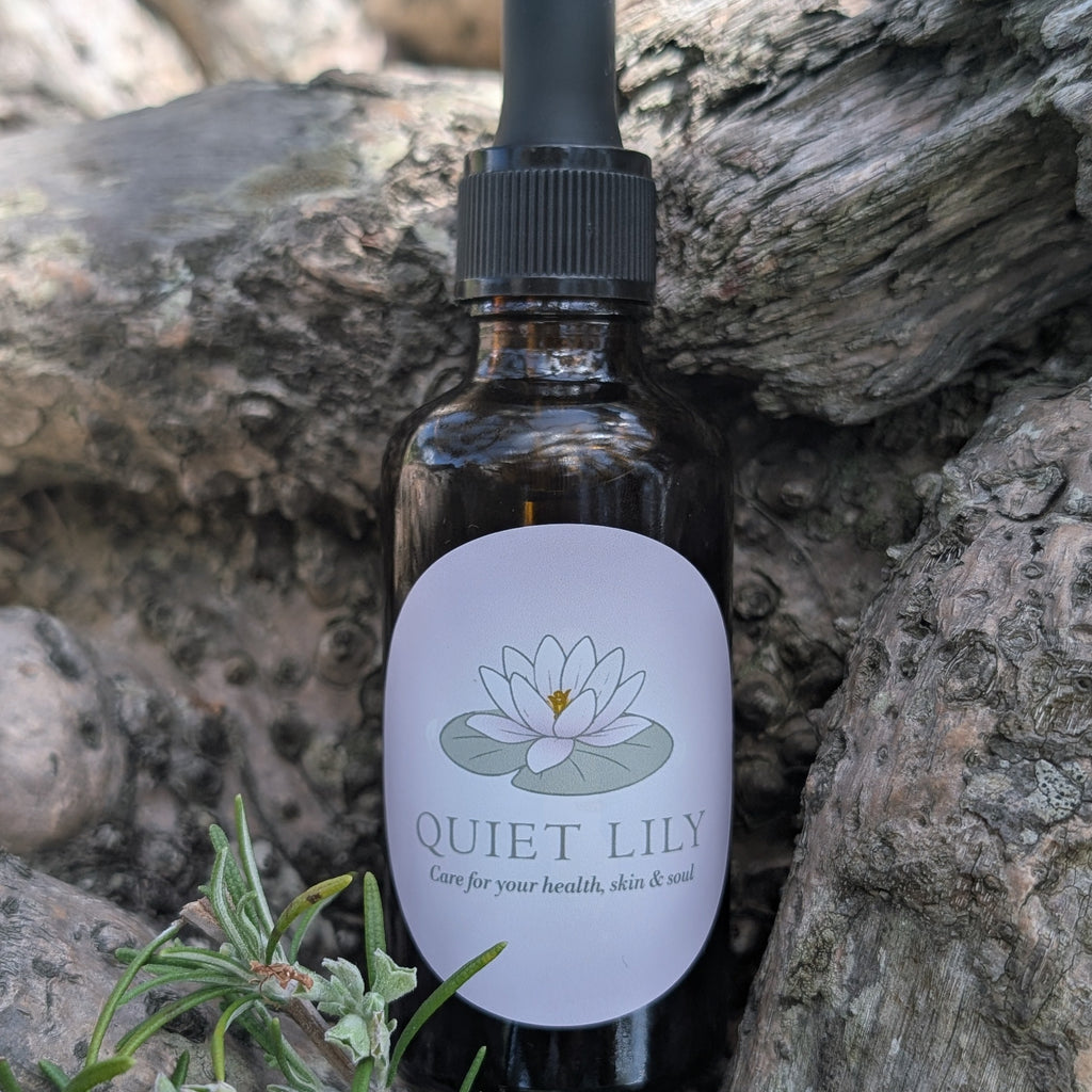 Bottle of 'Quiet Lily' product with a dropper on a stone background